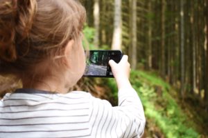 Image of a child using a cell phone to take video in the woods.