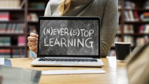 Image of someone holding a laptop with a chalkboard on the screen saying to never stop learning.